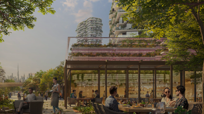 Une terrasse de café animée entourée de bois de ghaf et de bâtiments modernes avec des jardins verticaux. Les gens sont assis à des tables en train de prendre leurs repas et un serveur sert une table. Le ciel est clair avec quelques nuages et un horizon lointain de la ville est visible en arrière-plan.