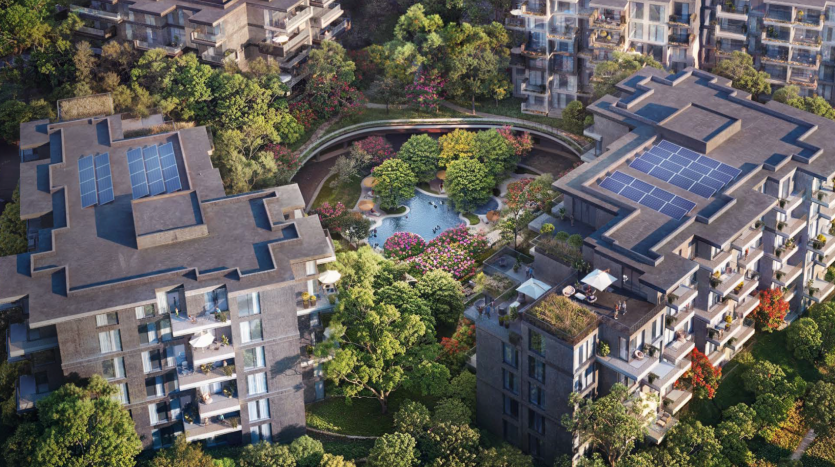 Vue aérienne d'un complexe résidentiel luxueux comprenant plusieurs immeubles d'appartements modernes, dotés de panneaux solaires sur les toits. Le complexe est entouré d'une verdure luxuriante, d'arbres et de jardins paysagers nichés dans les bois sereins de Ghaf, comprenant un plan d'eau central avec des plantes à fleurs vibrantes.