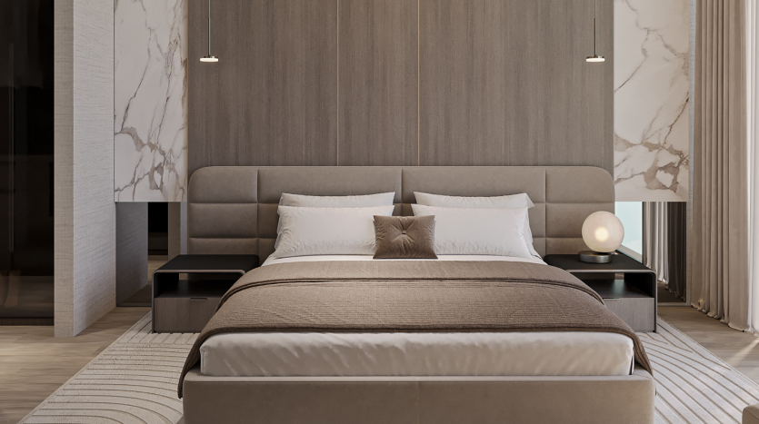 Une chambre moderne du Primero Residences Al Furjan comprend un grand lit avec une literie et des oreillers beiges, placé contre un mur lambrissé. Deux tables de nuit, chacune avec une lampe, flanquent le lit. Les accents de marbre et les rideaux allant du sol au plafond se combinent pour créer un design élégant et minimaliste.