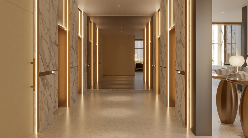 Un couloir moderne et bien éclairé avec des murs en marbre et des accents de lumière chaleureuse. Le couloir est flanqué d’élégantes portes en bois aux lignes épurées. Au bout du couloir, on aperçoit une pièce spacieuse avec de grandes fenêtres et un mobilier contemporain, mettant en valeur la sophistication de Primero Residences Al Furjan.