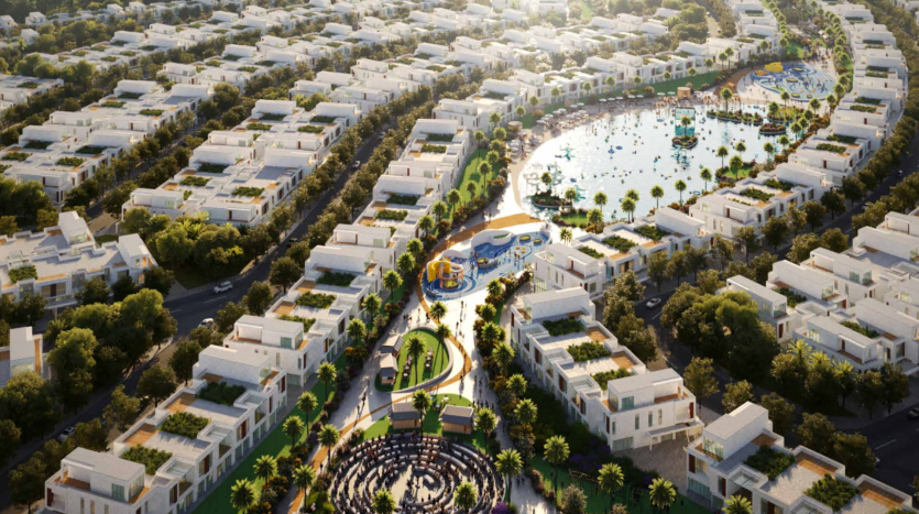 Vue aérienne d&#039;un quartier résidentiel moderne du sud de Dubaï avec de nombreux bâtiments blancs, une verdure luxuriante et un lac central entouré de palmiers et de sentiers pédestres. Aire de jeux centrale colorée et jardins paysagers visibles.