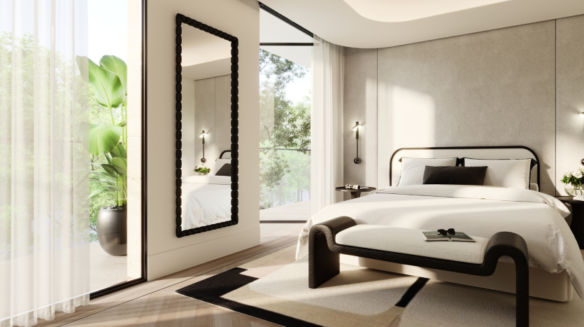 Chambre moderne de la Villa Karl Lagerfeld avec un grand lit, des oreillers noirs et blancs, un miroir au sol et une vue panoramique à travers une fenêtre avec des rideaux transparents. Une plante d&#039;intérieur ajoute une touche de