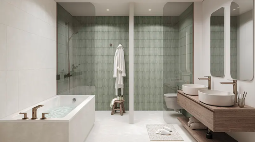 Salle de bains moderne comprenant une grande baignoire avec un rebord en bois et des luminaires en laiton, une douche à l'italienne avec des carreaux verts Verdes, des toilettes murales et une double vasque avec vasques, robinets en laiton et deux miroirs allongés. Un peignoir blanc est suspendu à côté de la douche.