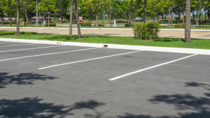 Un parking vide avec des lignes blanches fraîchement peintes, également appelés places de parking, est entouré d&#039;herbe verte, d&#039;arbres et de quelques buissons. Les ombres des arbres tombent sur l&#039;asphalte. Quelques voitures et une route sont visibles en arrière-plan au-delà de l&#039;herbe. Le décor évoque un coin étonnamment serein de Dubaï.