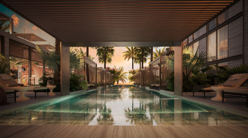 Une luxueuse piscine intérieure-extérieure du Berkeley comprend une pergola en bois moderne, flanquée de plantes tropicales et de chaises longues confortables. La piscine s'étend vers un horizon coucher de soleil avec des palmiers se reflétant sur l'eau, créant une atmosphère sereine et invitante.