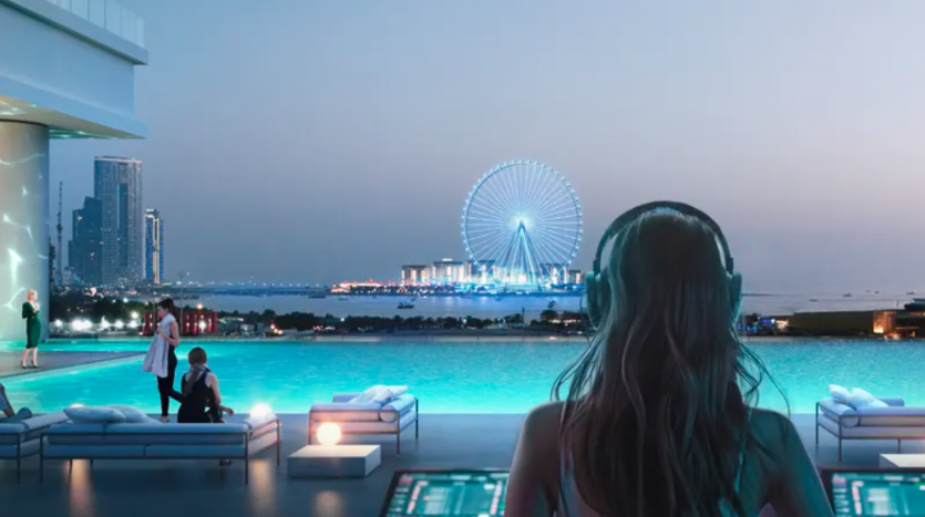 Une personne portant des écouteurs surplombe une piscine à débordement au crépuscule, avec des gratte-ciels et une grande roue illuminée en arrière-plan. D'autres personnes sont autour de la piscine, profitant de l'ambiance sereine et de l'espace de détente extérieur moderne.