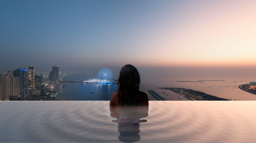 Une personne est représentée de dos, assise dans une piscine à débordement au crépuscule au W Residences Dubai Harbour. La vue donne sur les toits de la ville avec de grands immeubles, une grande roue illuminée et une mer calme sous un ciel dégradé passant du bleu au rose. Des ondulations entourent la personne dans l'eau.