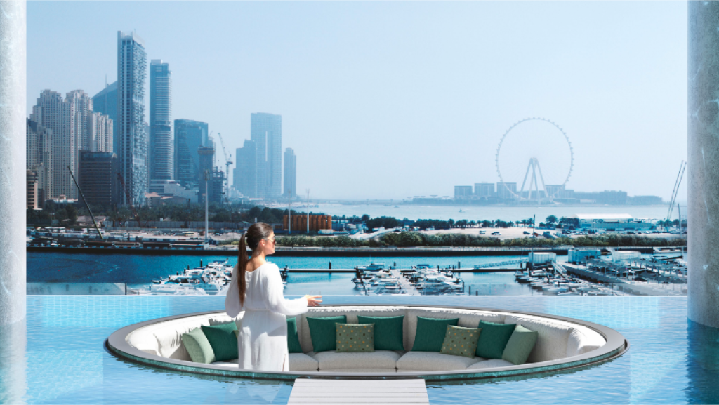 Une femme vêtue d'une robe blanche se tient dans un coin salon surélevé, circulaire et en contrebas, entouré d'eau dans le luxueux port de W Residences Dubai, surplombant une marina avec des bateaux et les toits de la ville. Une grande roue est visible au loin sur un ciel bleu clair.