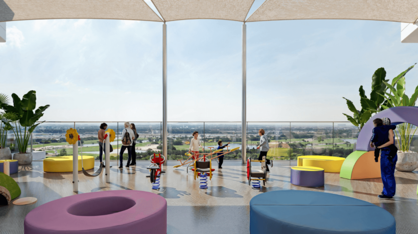 Enfants et adultes profitent d'une aire de jeux extérieure sur le toit des jardins Ayana, dotée d'équipements de jeux colorés et de grandes plantes en pot. La zone dispose de structures d'ombrage et offre une vue panoramique sur le paysage urbain, avec de la verdure et des bâtiments en arrière-plan.