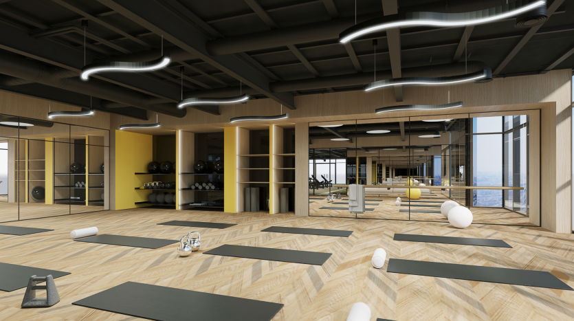 Un studio de yoga spacieux et moderne avec du parquet et de hauts plafonds comprend des tapis de yoga noirs alignés en rangées, de grands miroirs sur les murs et divers accessoires de yoga tels que des traversins, des blocs et des sangles. La pièce est bien éclairée grâce à la lumière naturelle abondante provenant de grandes fenêtres.