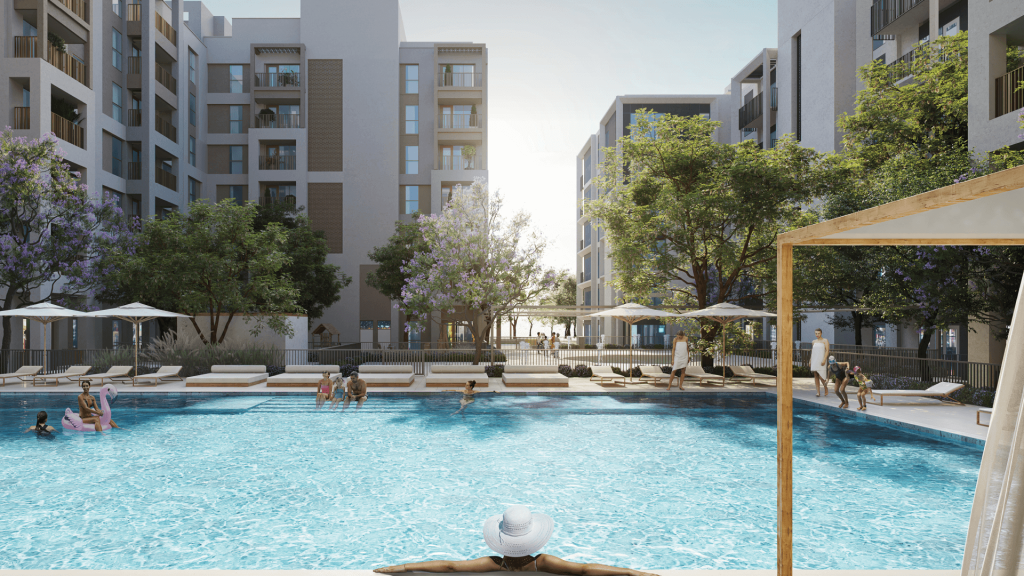 Une piscine extérieure sereine est entourée d'immeubles d'appartements modernes. Les gens se prélassent, nagent et profitent du soleil. Les arbres aux fleurs violettes et les parasols fournissent de l'ombre, créant un paysage pittoresque avec une ambiance lumineuse et relaxante.