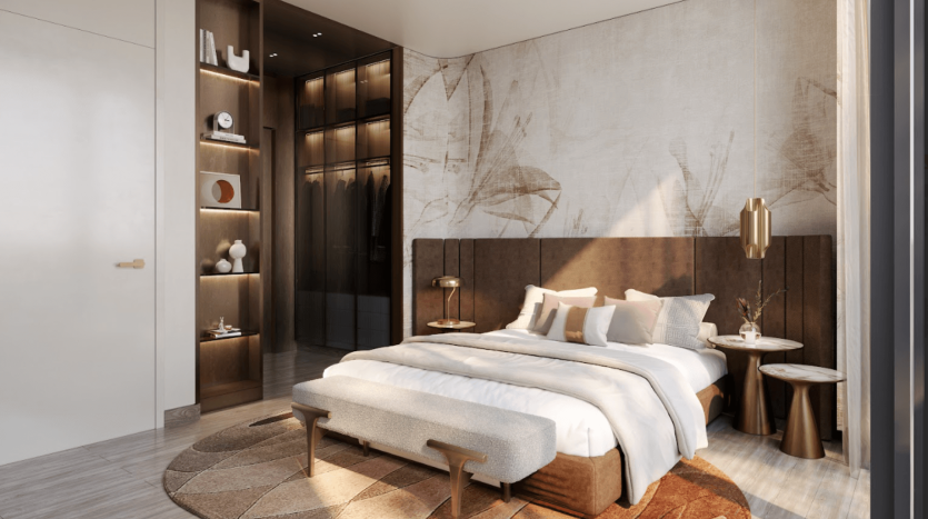 Chambre élégante du One Residences comprenant un grand lit avec une tête de lit rembourrée marron, entouré de meubles modernes en bois. Un dressing avec étagères ouvertes est visible. Des tons doux et neutres décorent la pièce, complétés par des œuvres d'art murales abstraites et un tapis confortable à motifs.