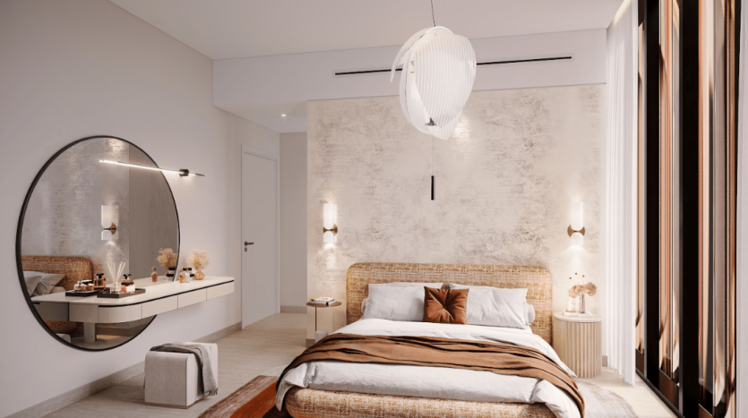 Une chambre moderne du One Residences comprend un lit avec un cadre en rotin et une literie superposée marron et crème. Deux tables d'appoint murales avec vases et décor encadrent le lit. Un miroir rond au-dessus d'une vanité flottante et un luminaire texturé ajoutent à l'ambiance élégante.