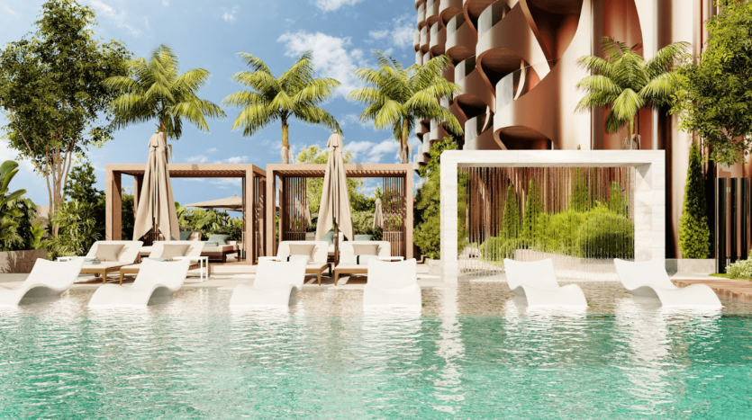 Scène luxueuse au bord de la piscine de One Residences, avec des chaises longues blanches immergées dans l'eau claire d'une piscine turquoise étincelante. Derrière eux se trouvent des cabanes et des palmiers sous un ciel bleu éclatant. Un bâtiment moderne au design géométrique unique se dresse en arrière-plan.