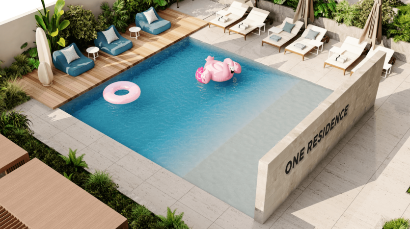 Une piscine rectangulaire moderne aux eaux bleu clair est entourée de chaises longues et de parasols. Un flamant rose gonflable et un anneau rose flottent dans la piscine. Un mur intitulé "One Residences" entoure un côté de la piscine, ornée de plantes vertes.