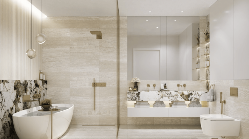 La salle de bains moderne du One Residences comprend une baignoire îlot, une douche murale et des toilettes en céramique blanche. Le design élégant comprend des murs et un sol en marbre beige, un grand miroir de courtoisie, des étagères flottantes décorées, ainsi que des luminaires et un éclairage dorés ajoutant une touche de luxe.