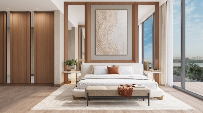 The modern bedroom at Belgrove Residences features a king-size bed with a white comforter and cushions set against a wooden headboard. Next to the bed are two matching bedside tables with plants. The room has bay windows offering a view of the sunny outdoor landscape.