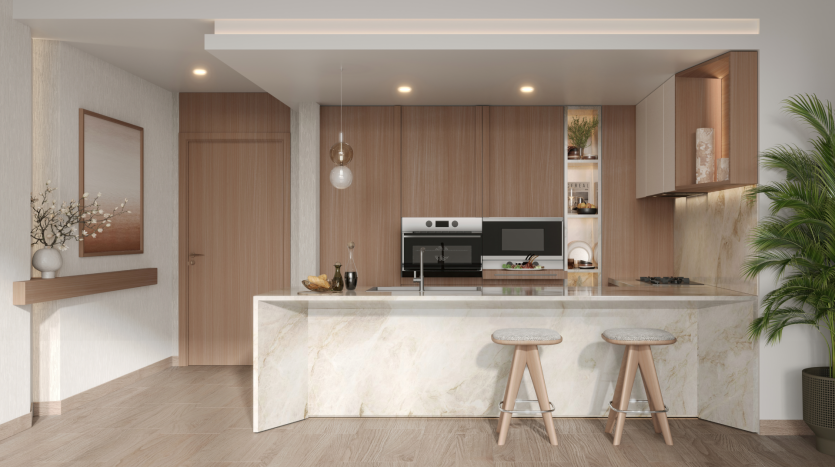 A modern kitchen in Belgrove residences features a marble island with two wooden stools, paneled cabinetry, integrated stainless steel appliances and subdued overhead lighting. Decorative elements such as a plant, a work of art and a vase with branches add charm to the space.