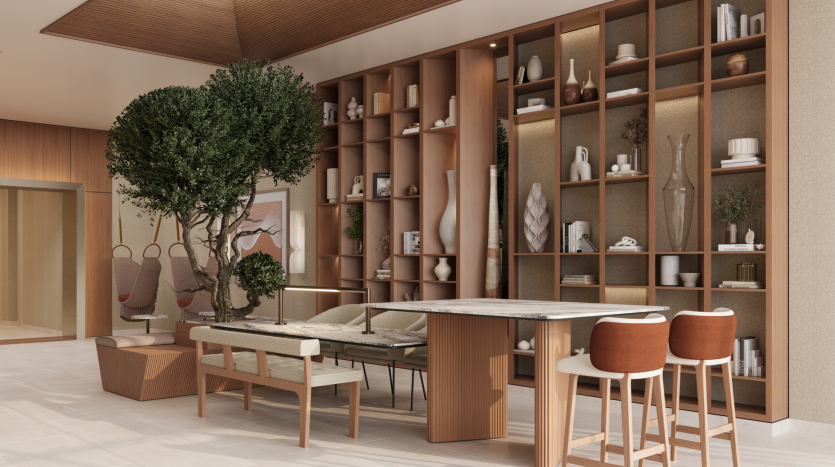 A modern, stylish room at Belgrove Residences features a wooden bookcase filled with decorations, books and plants. The room includes a table with bar stools, a bench with a marble table and an indoor tree. Neutral tones and wooden accents create a warm, welcoming atmosphere.