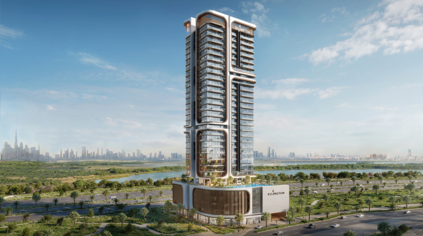 A modern, high-rise skyscraper of intricate design stands against a clear blue sky and the city's rooftops in the distance. The building, known as Belgrove Residences, is surrounded by greenery and a few roads, and bears a sign reading "Ellington" near its base.