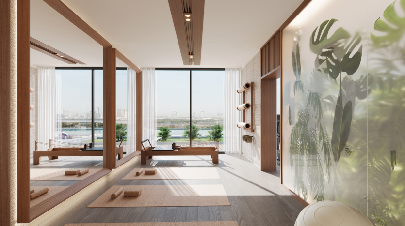 The sunny, modern yoga studio at Belgrove Residences has large windows offering views of the cityscape. The room features parquet flooring, yoga mats and equipment, including carefully arranged blocks and straps. A mirrored wall reflects the opposite green-painted wall, reinforcing the serene ambience.