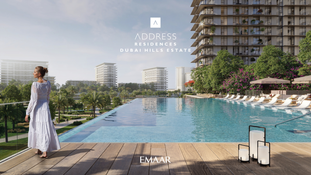 A woman in a white dress stands by an infinity pool overlooking Address Residences Dubai Hills. The view features modern high-rise buildings, lush vegetation and poolside loungers. Two decorative lanterns sit on the wooden terrace, adding a touch of elegance to the serene scene.