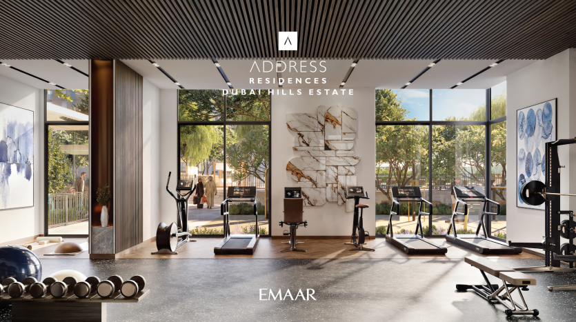 A modern gym with large windows revealing the greenery outside. Inside you'll find a variety of exercise machines, including treadmills, stationary bikes and weights. The interior is elegantly decorated with wooden accents and artwork on the walls. This is the fitness center of Address Residences Dubai Hills Estate Emaar.