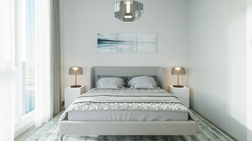 Une chambre moderne avec un grand lit centré contre un mur blanc, flanqué de deux tables de nuit blanches avec des lampes assorties. Au-dessus du lit est suspendu un triptyque abstrait bleu et blanc. La pièce est dotée de baies vitrées, d'un tapis gris et d'une suspension géométrique d'inspiration centenaire.