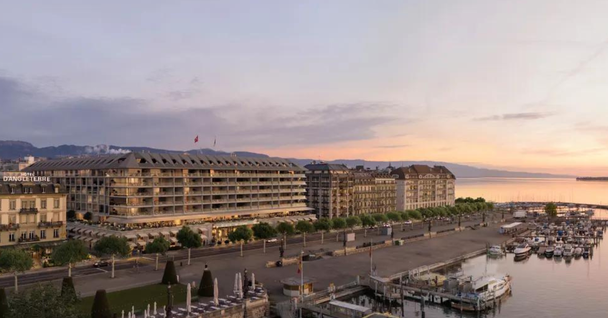 Vue panoramique d'un front de mer au coucher du soleil, avec des bateaux amarrés à une marina. En arrière-plan, on distingue plusieurs grands bâtiments, dont un avec une enseigne « D'ANGLETERRE ». La beauté du ciel orange et violet reflète le charme que l'on pourrait trouver dans un salon bruxellois.