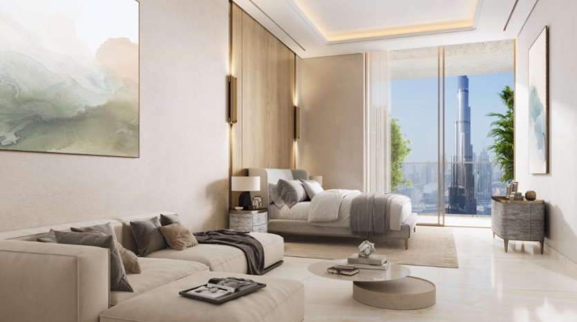 Une chambre moderne et spacieuse du Fairmont Residences comprend un grand lit, un canapé beige confortable et une décoration minimaliste. Les baies vitrées offrent une vue imprenable sur le paysage urbain, notamment sur un gratte-ciel proéminent. La lumière naturelle illumine la pièce, mettant en valeur la palette de couleurs neutres et le mobilier élégant.