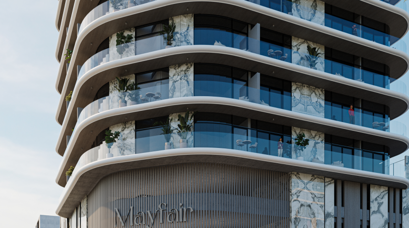 Un bâtiment architectural moderne avec des murs extérieurs incurvés et de vastes balcons en verre. La façade présente un mélange de panneaux gris lisses et d'accents à motifs de marbre. Le nom « Mayfair » est visible à la base du bâtiment.