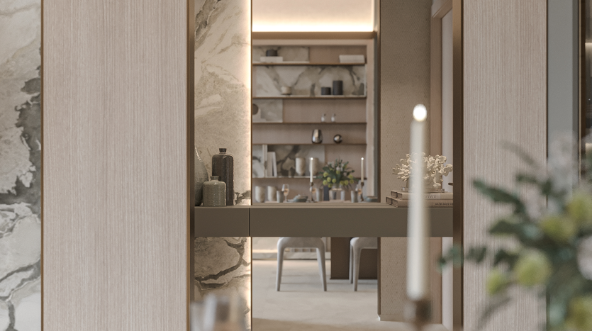 Intérieur moderne comprenant un couloir avec des murs en marbre et des boiseries. Un comptoir flottant orné de bougies et de décorations mène à un salon décoré avec goût avec une bibliothèque et une table à manger. Une plante floue et une bougie au premier plan créent de la profondeur.