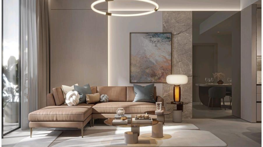 A modern living room with a beige corner sofa adorned with gray and white cushions, a round coffee table, a large abstract painting on the wall and a circular hanging lamp. The Legado Prescott-themed space features a large window with sheer curtains and an adjacent dining room visible in the background.