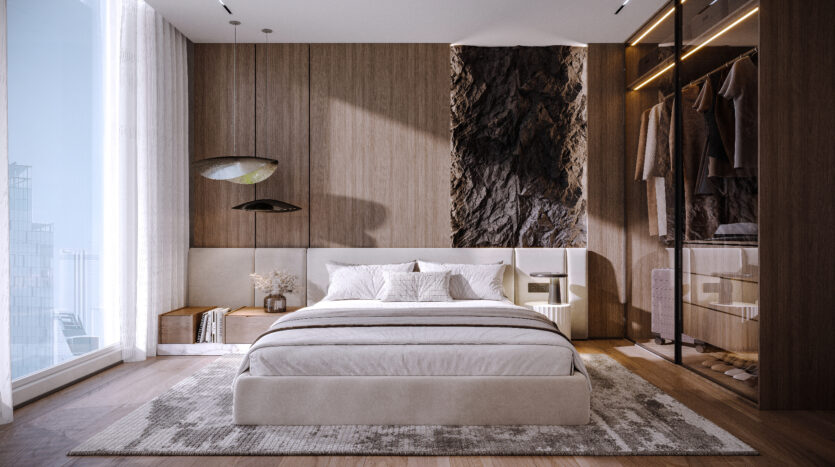 A modern room at Allura Residences features a quilted bed with white linens, flanked by elegant nightstands. Earth-toned walls highlight a textured panel. Soft natural light fills the space through large windows next to a minimalist wardrobe with glass doors. A rug covers part of the parquet floor.