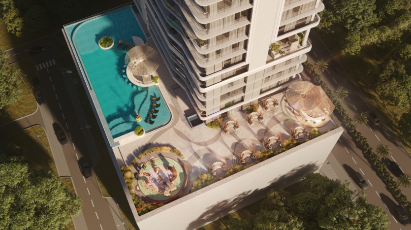 Aerial view of Allura Residences, a modern multi-storey building with a rooftop leisure area. The rooftop features a large swimming pool, relaxation areas with deckchairs and landscaped green spaces. Adjacent roads and lush trees surround the building, providing a serene environment.