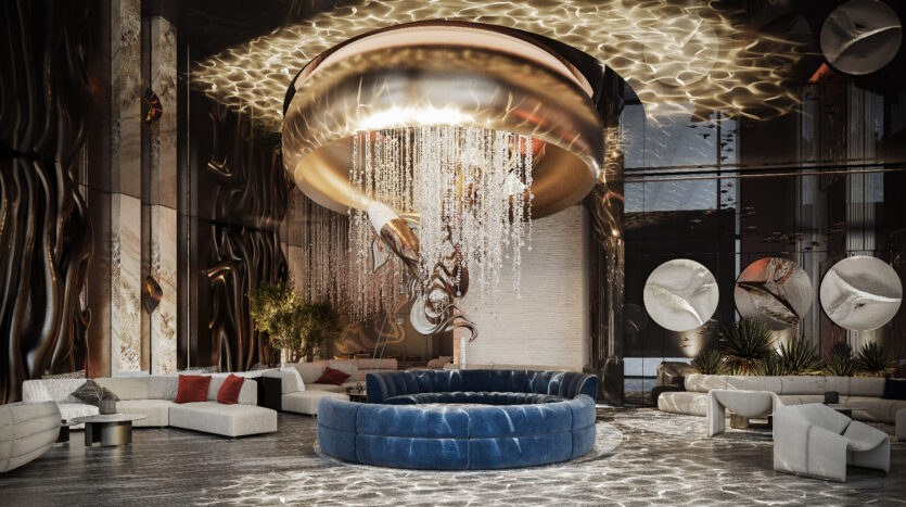 The lobby of Allura Residences exudes luxury with its large circular blue sofa, modern gray and white seating and chandelier adorned with cascading crystal elements. Abstract metallic artwork adorns the walls, while large windows let natural light into the space.