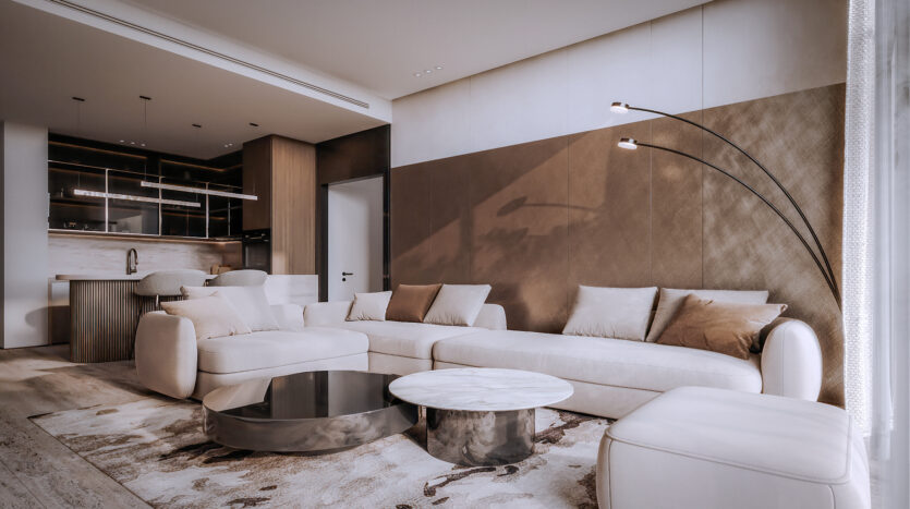 Allura Residences offers a modern living room featuring a large beige corner sofa adorned with neutral cushions, two round coffee tables and an arched floor lamp with two lights. The space opens onto a stylish kitchen with dark cabinetry and an elegant island with bar stools.