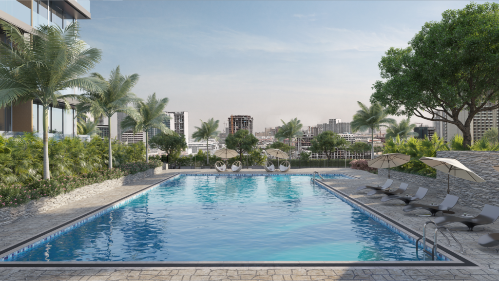 Une piscine extérieure entourée de palmiers et de chaises longues avec parasols. En arrière-plan, les 2 bâtiments modernes Skyhills se dressent sur un ciel dégagé. La zone au bord de la piscine est pavée de carreaux de pierre, créant un environnement serein et accueillant.