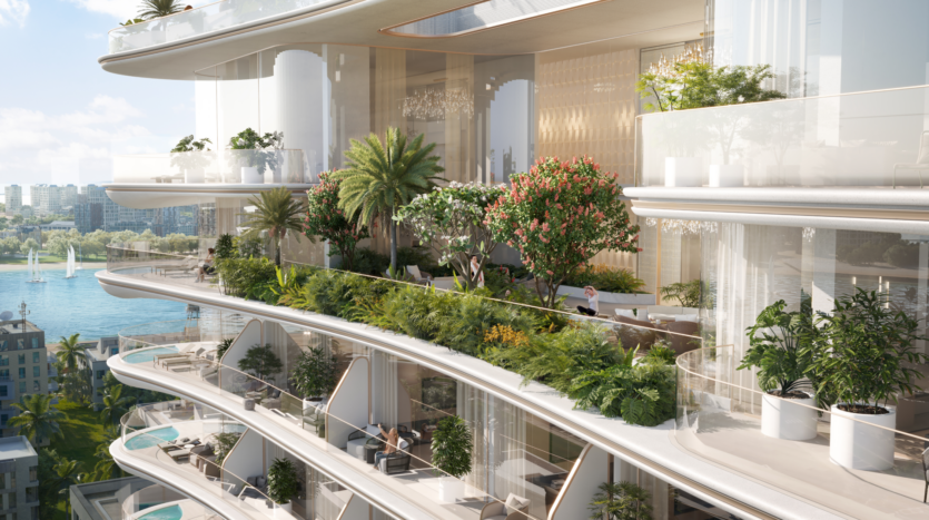 Un immeuble de luxe à plusieurs niveaux avec de grands balcons remplis de verdure luxuriante, de palmiers et de plantes. Les balcons donnent sur un plan d'eau avec des voiliers et un horizon de la ville voisine en arrière-plan. On voit des gens se détendre et profiter de l'environnement serein de Beach Walk 3.