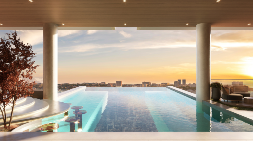 A luxurious infinity pool, designed by Allura Citi Developers, graces a high terrace overlooking the cityscape at sunset. Submerged bar stools and elegant seating surround the oasis, where a solitary tree stands against a sky painted in soft orange and blue tones.