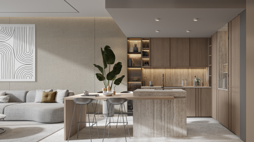 La cuisine moderne du One Beverly Dubai est dotée d'armoires en bois, d'un îlot en marbre avec deux tabourets et d'étagères intégrées avec des objets décoratifs. L'agencement ouvert comprend un salon confortable avec un canapé gris et des œuvres d'art murales abstraites. Une grande plante en pot sur l'îlot ajoute une touche de verdure.