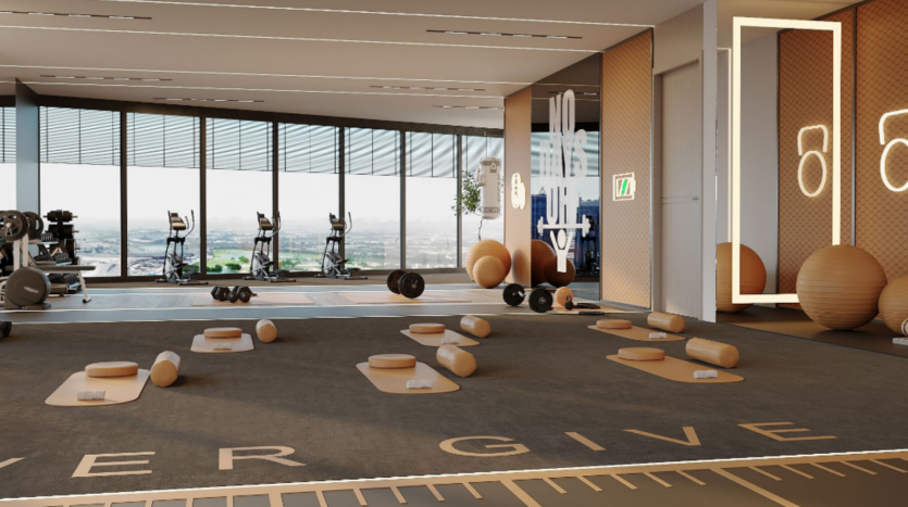 Un studio de fitness moderne avec de grandes fenêtres donnant sur un paysage urbain. La salle comprend des vélos stationnaires, des haltères, des ballons d'exercice et un mur en miroir. Des tapis de yoga avec des blocs et des coussins sont disposés sur le sol. Les mots « NE JAMAIS DONNER » sont partiellement visibles sur le sol.