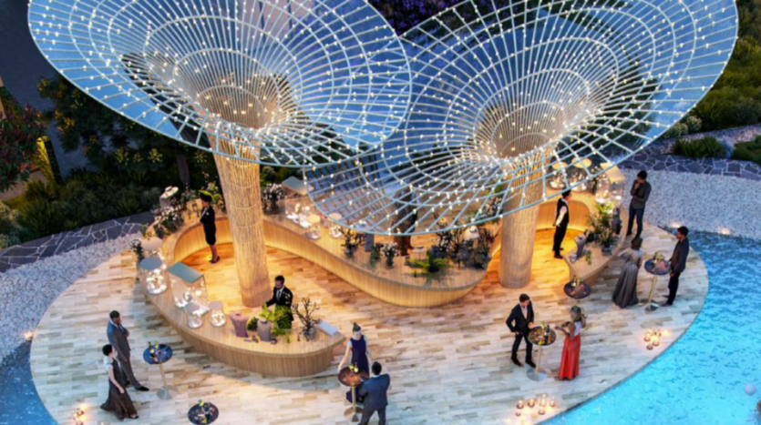 Vue aérienne d'un événement élégant en plein air au bord d'une piscine au crépuscule à Sun City. Les invités en tenue de soirée discutent autour d'un bar en bois orné de lumières et de deux grandes structures à baldaquin artistiques. L'éclairage du soir ajoute une ambiance sophistiquée.