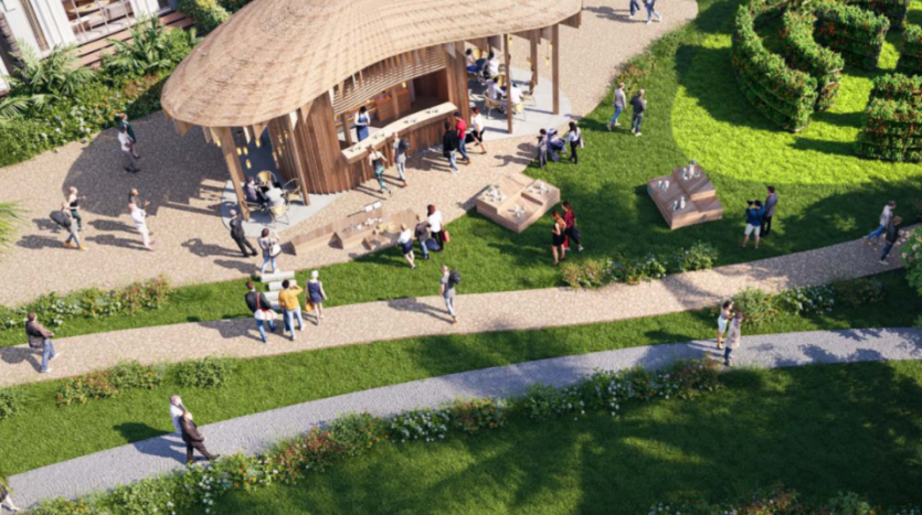 Vue aérienne du parc de Sun City avec un pavillon central en bois et des zones de sièges recouvertes d'herbe. Les gens sont rassemblés autour du pavillon et assis sur l'herbe. Des chemins de gravier serpentent à travers la verdure paysagère, et une petite section d'un labyrinthe de haies est visible sur la droite.