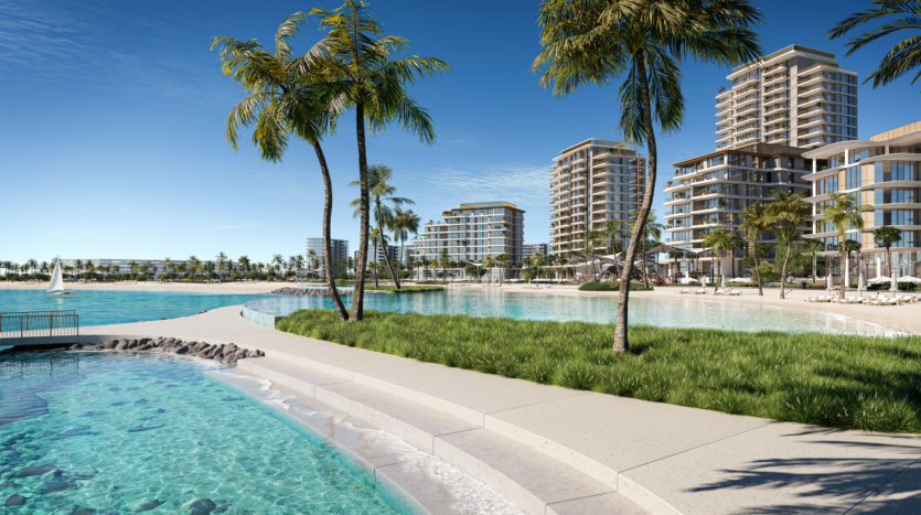 Une scène côtière avec des immeubles modernes de grande hauteur, des plages de sable, des eaux turquoise claires et des palmiers sous un ciel bleu vif. Une promenade bordée d'herbe longe le bord de l'eau, avec un petit voilier visible sur l'eau.