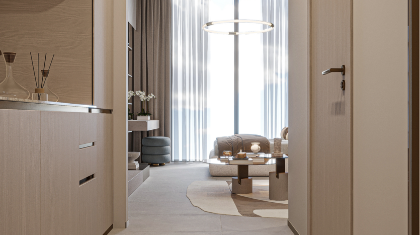 A modern interior hallway leads to a living room with a large window, sheer curtains, a circular chandelier, beige furniture and a patterned rug. Scented sticks and decorative objects sit on a side table.