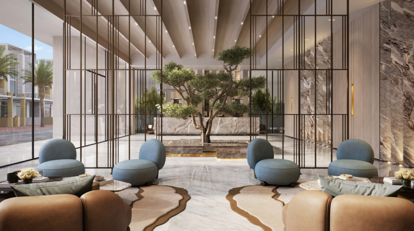 A modern hotel lobby with elegant marble flooring and large glass panels. Blue and brown upholstered seating surrounds a central area with a tree and plants. Natural light streams in through large windows, creating a bright, welcoming atmosphere.