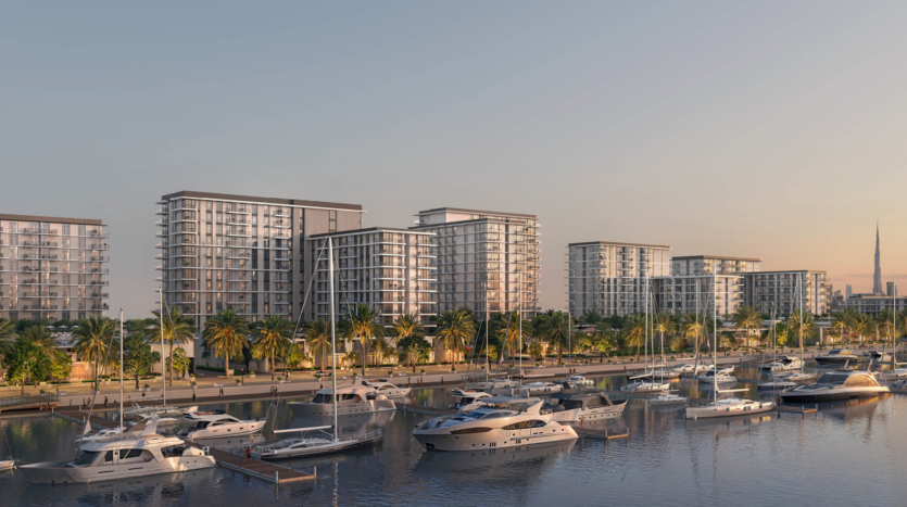 Une rangée d'appartements modernes en hauteur avec balcons surplombe une marina remplie de yachts à Pierpoint. Des palmiers bordent le front de mer et l'horizon lointain de la ville est visible dans un ciel clair en soirée.