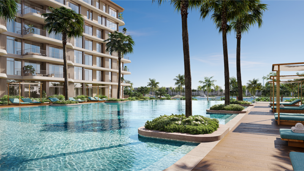 Un luxueux espace piscine extérieur entouré de palmiers, avec des chaises longues et des cabanes sur une terrasse en bois. À côté de la piscine se trouve un immeuble moderne de grande hauteur avec des balcons. Le ciel est clair et bleu, suggérant une journée ensoleillée.