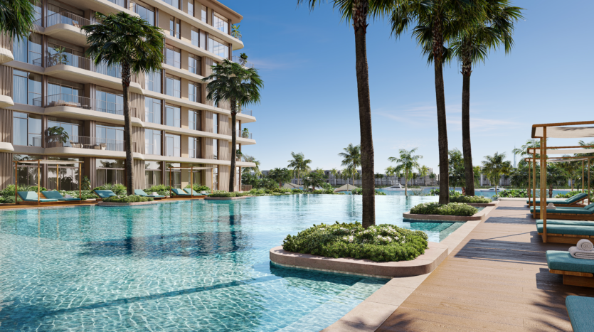 Un luxueux espace piscine extérieur entouré de palmiers, avec des chaises longues et des cabanes sur une terrasse en bois. À côté de la piscine se trouve un immeuble moderne de grande hauteur avec des balcons. Le ciel est clair et bleu, suggérant une journée ensoleillée.